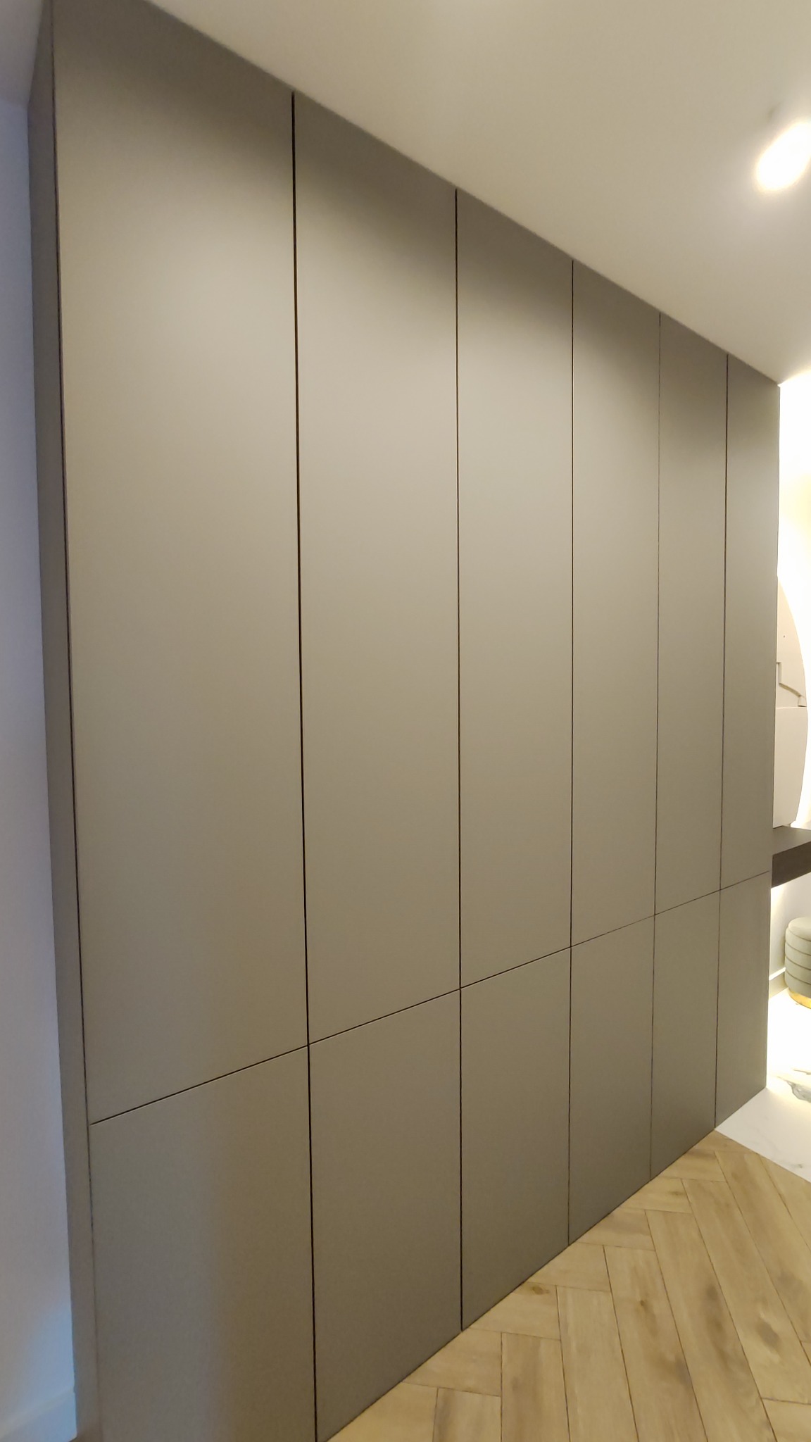 Szara szafa wnękowa z minimalistycznymi frontami, widoczna pod kątem, z parkietem ułożonym w jodełkę na podłodze.