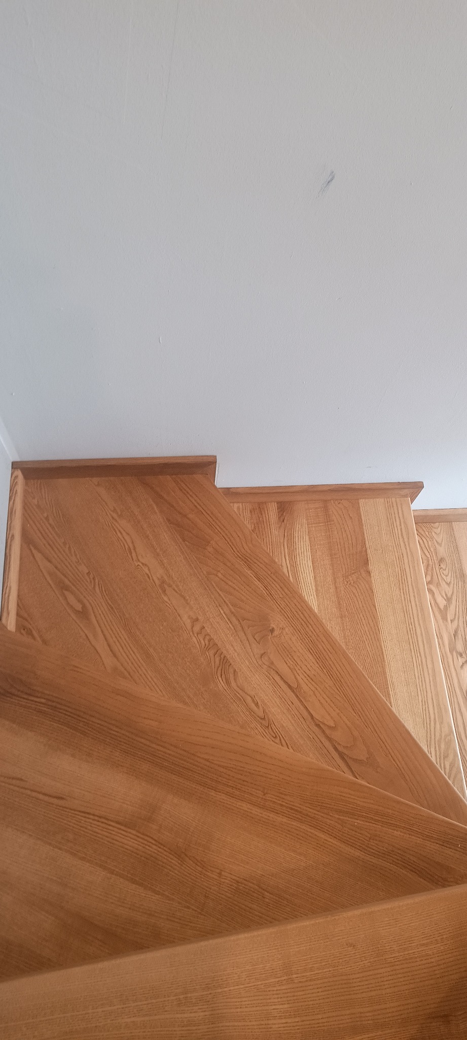 Widok z góry na stopnie z jasnego drewna, z widocznym rysunkiem słojów i białym sufitem w tle, ujęcie podkreśla naturalny charakter materiału.