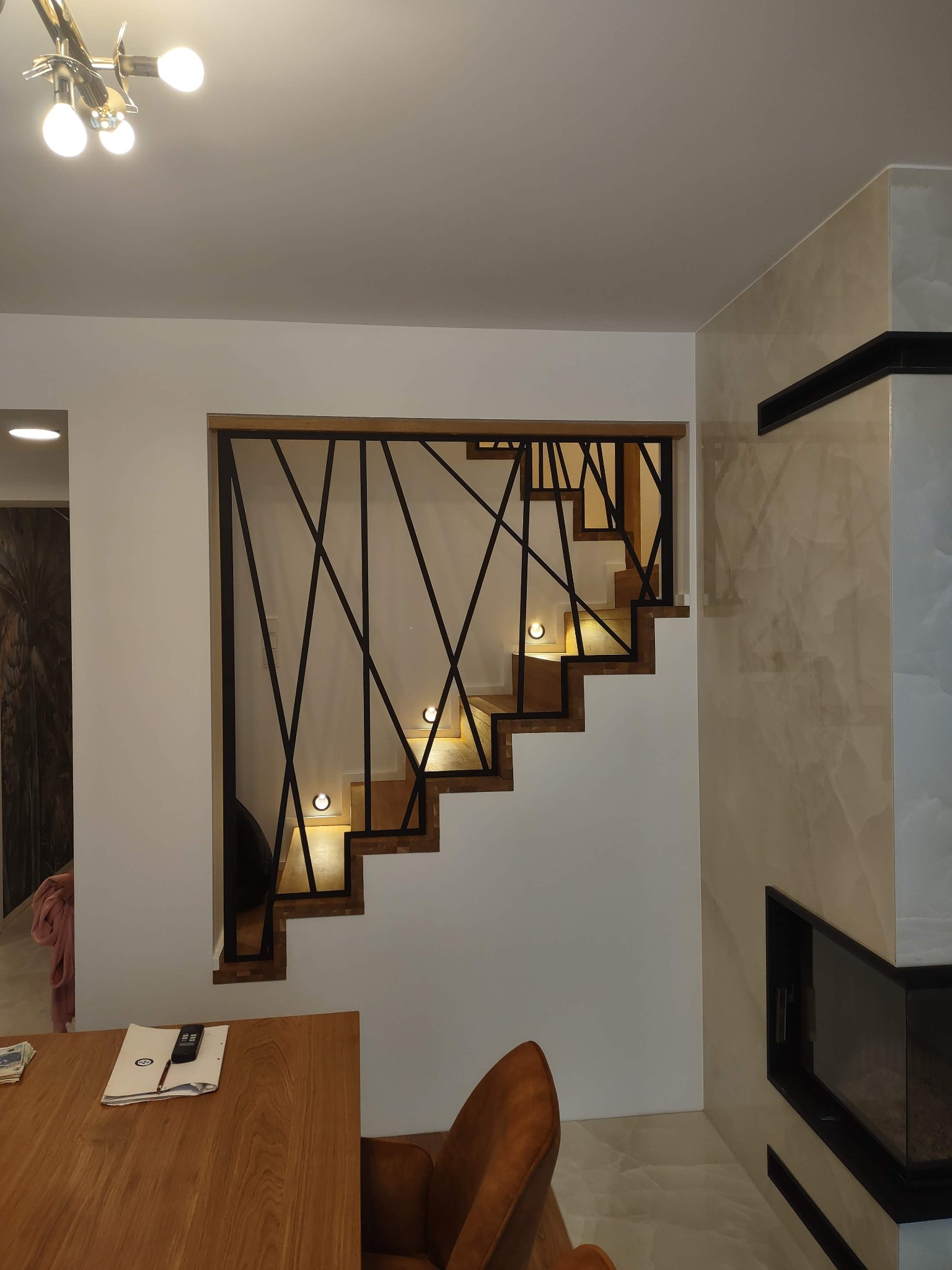 Nowoczesne schody z drewnianymi stopniami i czarną, geometryczną balustradą, oświetlone punktowo. Realizacja w Orzeszu. Minimalistyczny design.