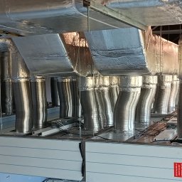 WRG Solutions - Widok od dołu na system kanałów wentylacyjnych z izolacją termiczną i centralę wentylacyjną z napisem 'All accessories are included in this package'.