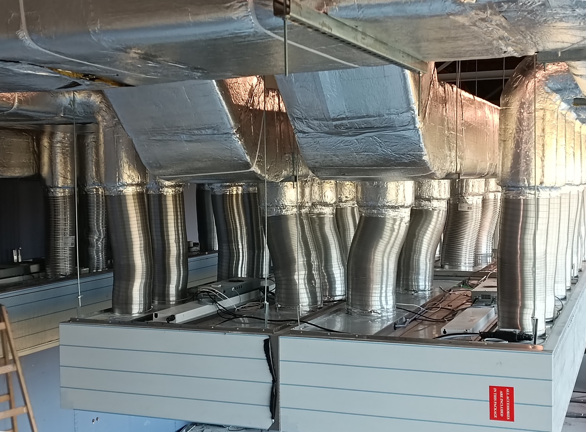 Widok od dołu na system kanałów wentylacyjnych z izolacją termiczną i centralę wentylacyjną z napisem 'All accessories are included in this package'.