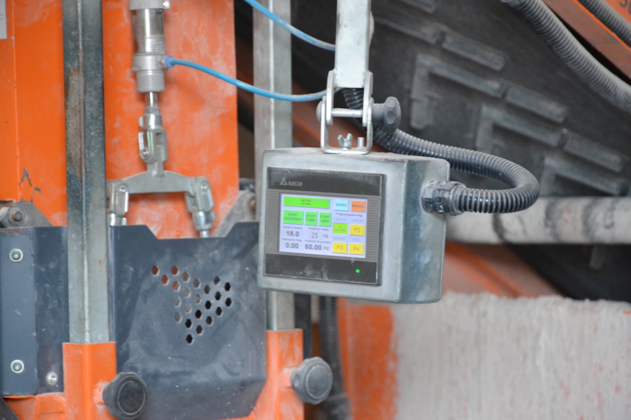 Panel sterowania z ekranem LCD, pokazujący parametry pracy maszyny budowlanej, z widocznymi przewodami i elementami konstrukcyjnymi.