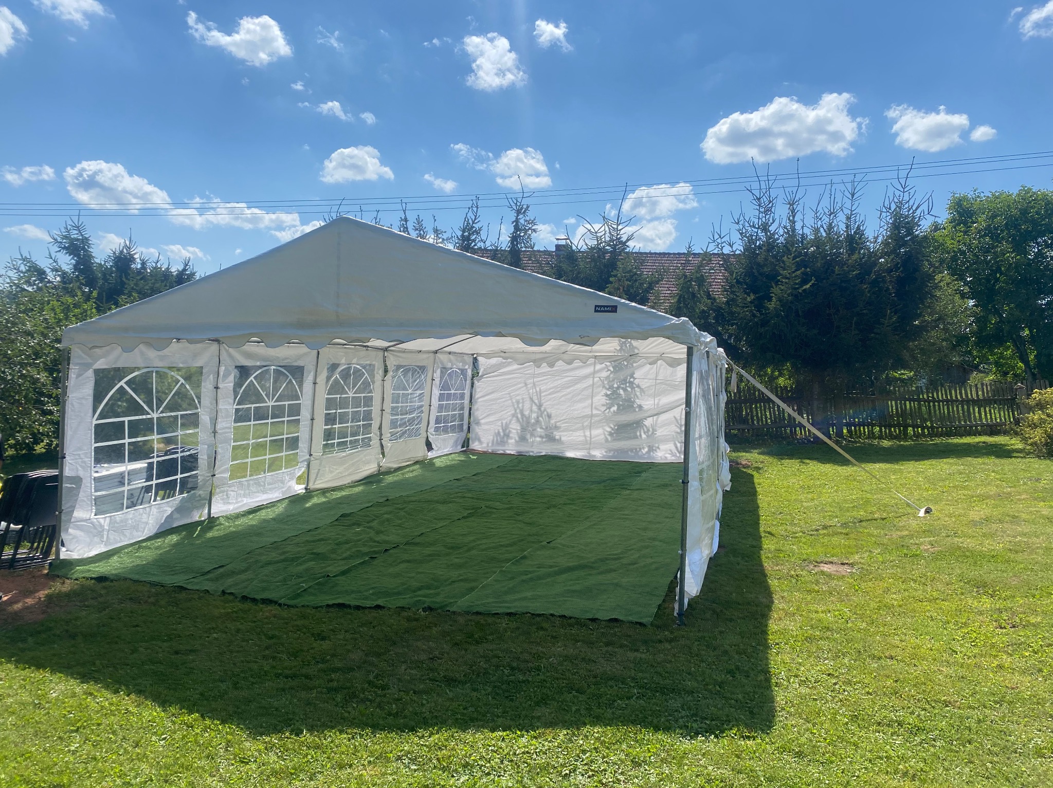 Biały namiot imprezowy rozstawiony na trawie, z zieloną wykładziną wewnątrz, widok w słoneczny dzień.