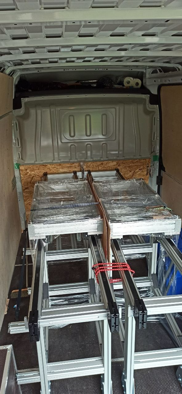 Transport aluminiowych konstrukcji pod panele fotowoltaiczne w przestrzeni ładunkowej busa, zabezpieczone folią i spięte czerwoną gumą.