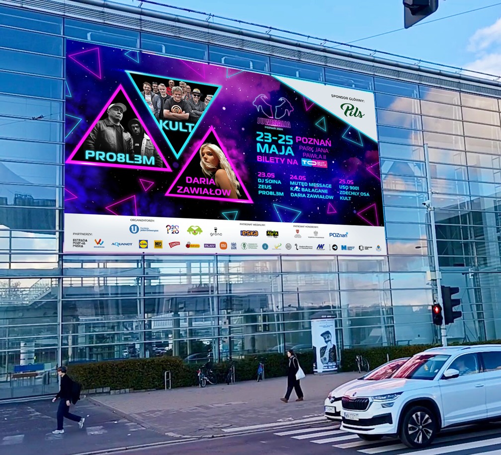 Wielkoformatowy baner reklamowy Juwenaliów Poznań 2024 z wizerunkami artystów i informacjami o wydarzeniu, umieszczony na fasadzie budynku, widoczny z perspektywy ulicy z przechodniami i samochodami.