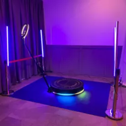 Oświetlona platforma obrotowa 360 z barierkami i ringiem świetlnym, ustawiona na ciemnoniebieskim dywanie, w pomieszczeniu z fioletowym oświetleniem.