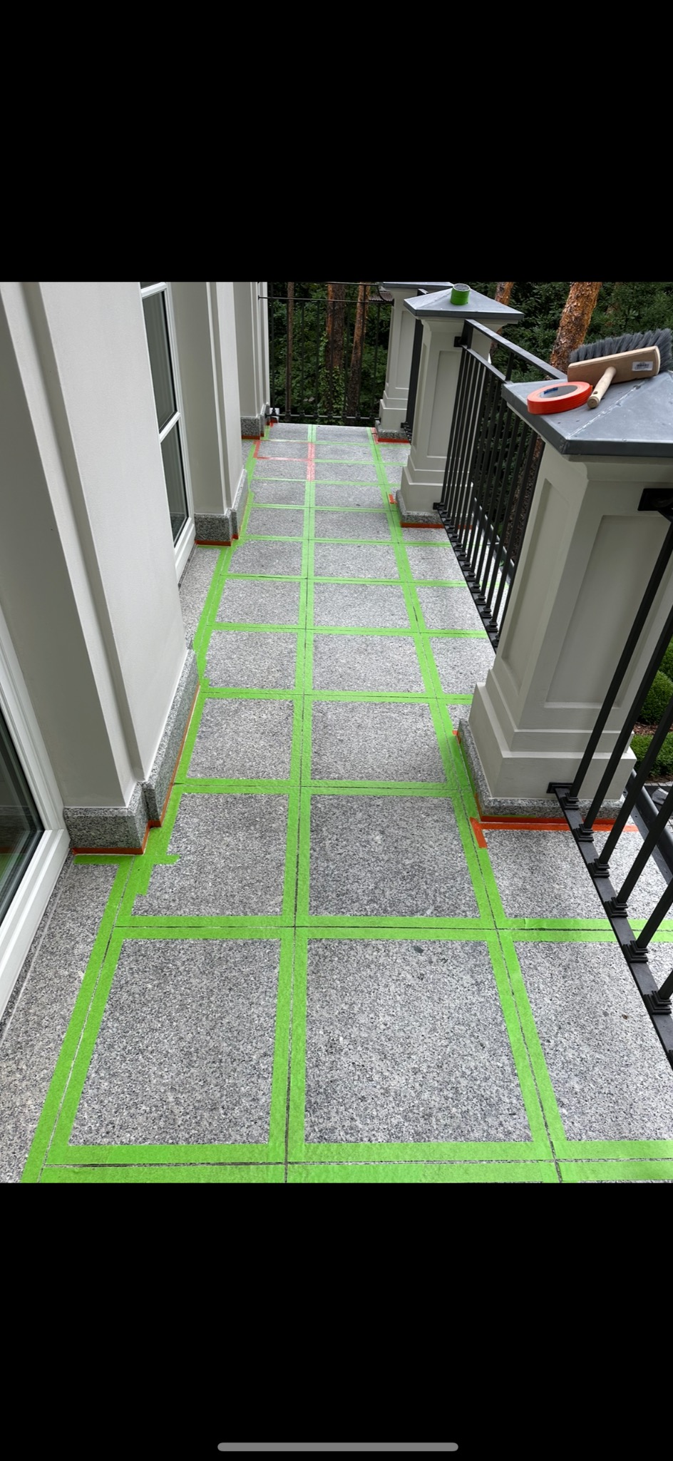 Przygotowanie powierzchni balkonu z szarego kamienia do prac wykończeniowych, zaznaczone pola zieloną taśmą, na balustradzie leży pędzel i taśma miernicza.