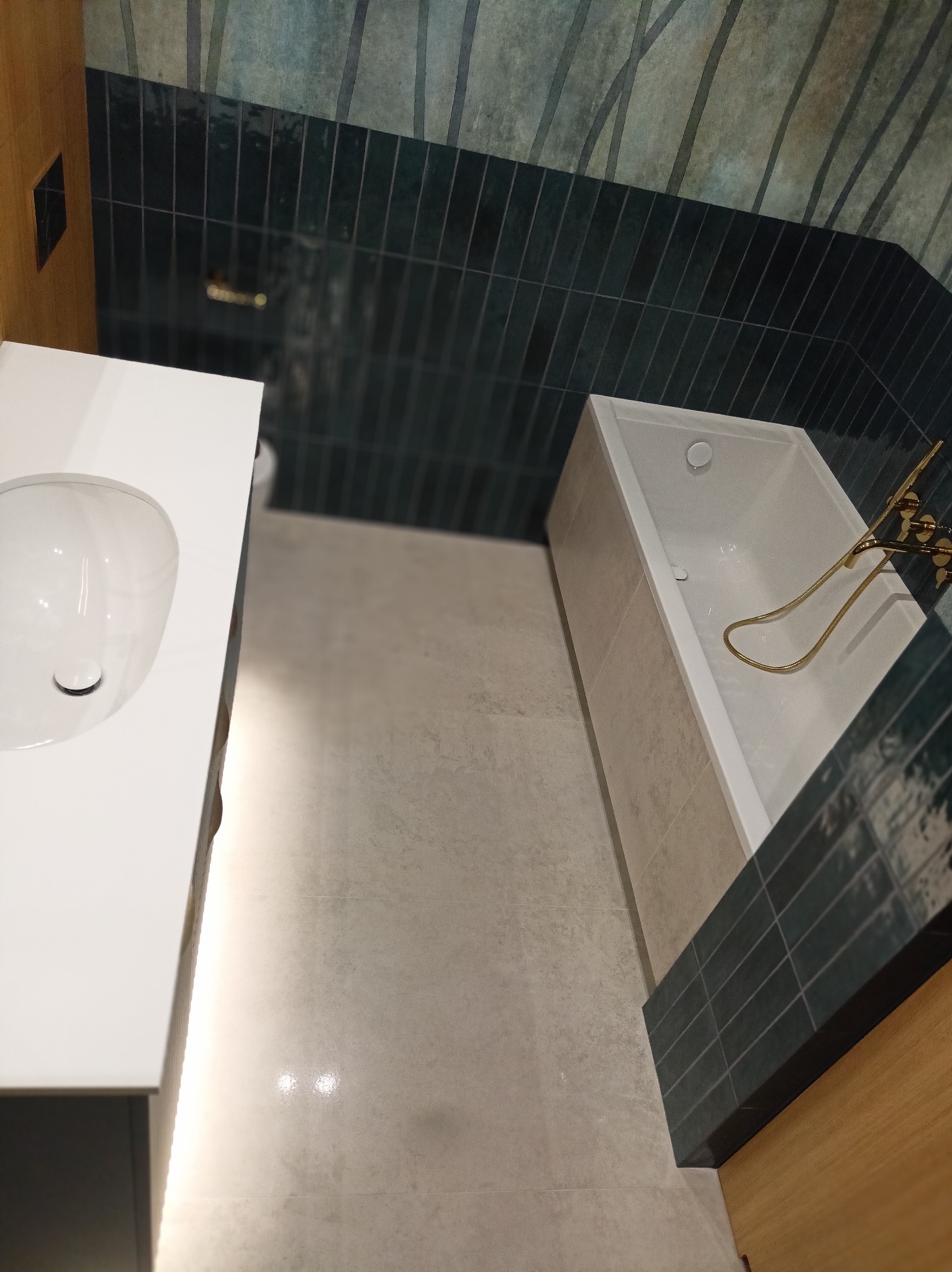 Nowoczesna łazienka z umywalką na blacie, wanną z złotą armaturą i ciemnymi płytkami imitującymi bambus na ścianie.
