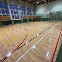 Sala gimnastyczna z parkietem po renowacji. Widoczne linie boiska w kolorach: żółtym, czerwonym, białym i czarnym. Parkiet błyszczący, ściany zielone.