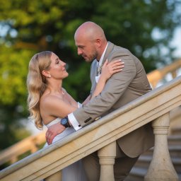 Rafał Torbicki Fotografia - Para młoda na marmurowych schodach, on w beżowym garniturze, ona w białej sukni, patrzą na siebie z miłością. Romantyczna sceneria ślubna.