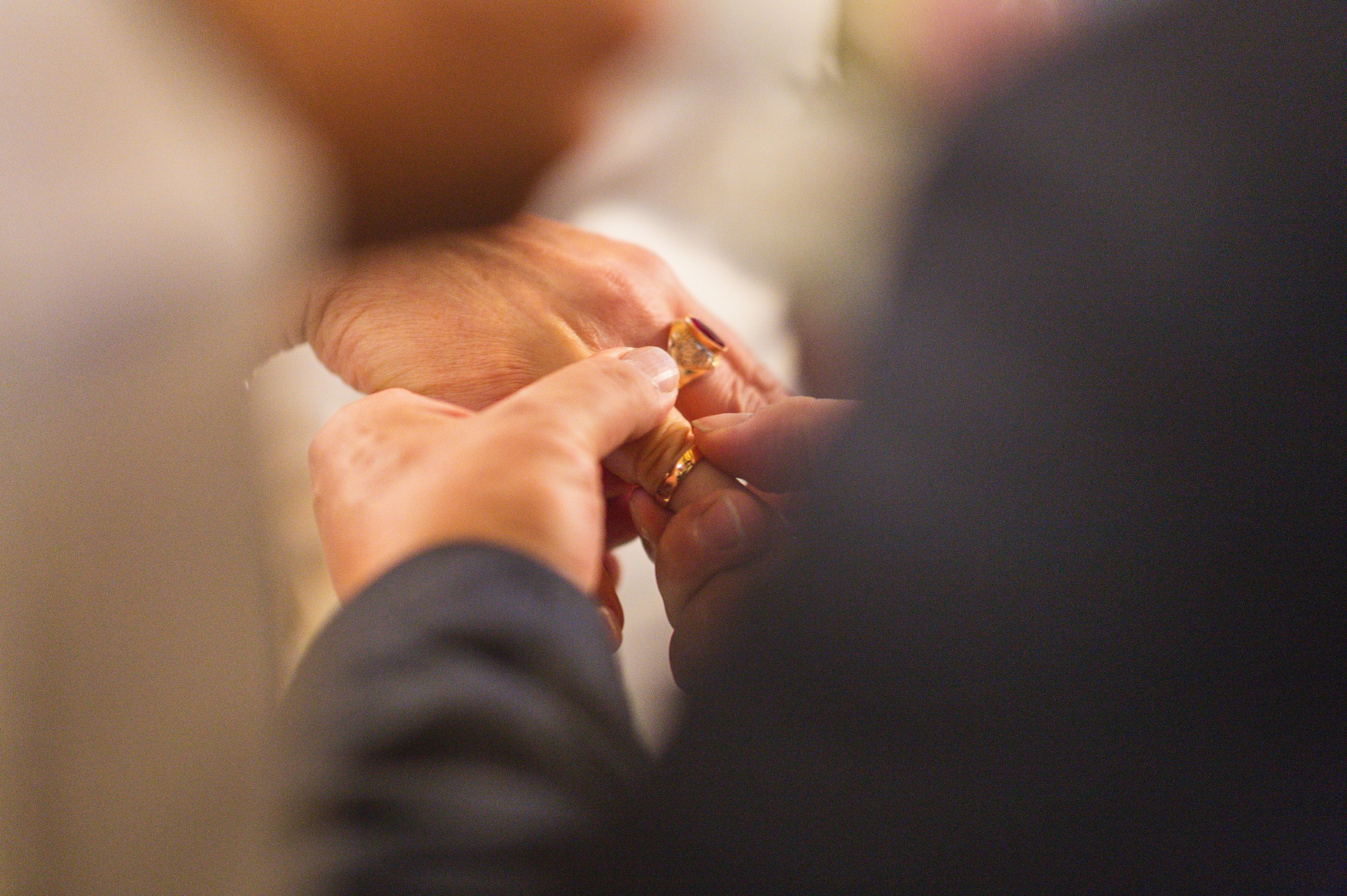Zbliżenie dłoni nakładających obrączkę z rubinowym oczkiem na palec panny młodej podczas ceremonii ślubnej, z rozmytym tłem sukni i garnituru.