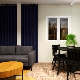 DYNAMIC ENGLISH LANGUAGE SERVICES SPÓŁKA Z OGRANICZONĄ ODPOWIEDZIALNOŚCIĄ - Wizualizacja salonu z szarą sofą narożną, okrągłym drewnianym stolikiem kawowym, czarnym okrągłym stołem jadalnym z krzesłami w stylu vintage oraz ścianą z cegły i dużym oknem.