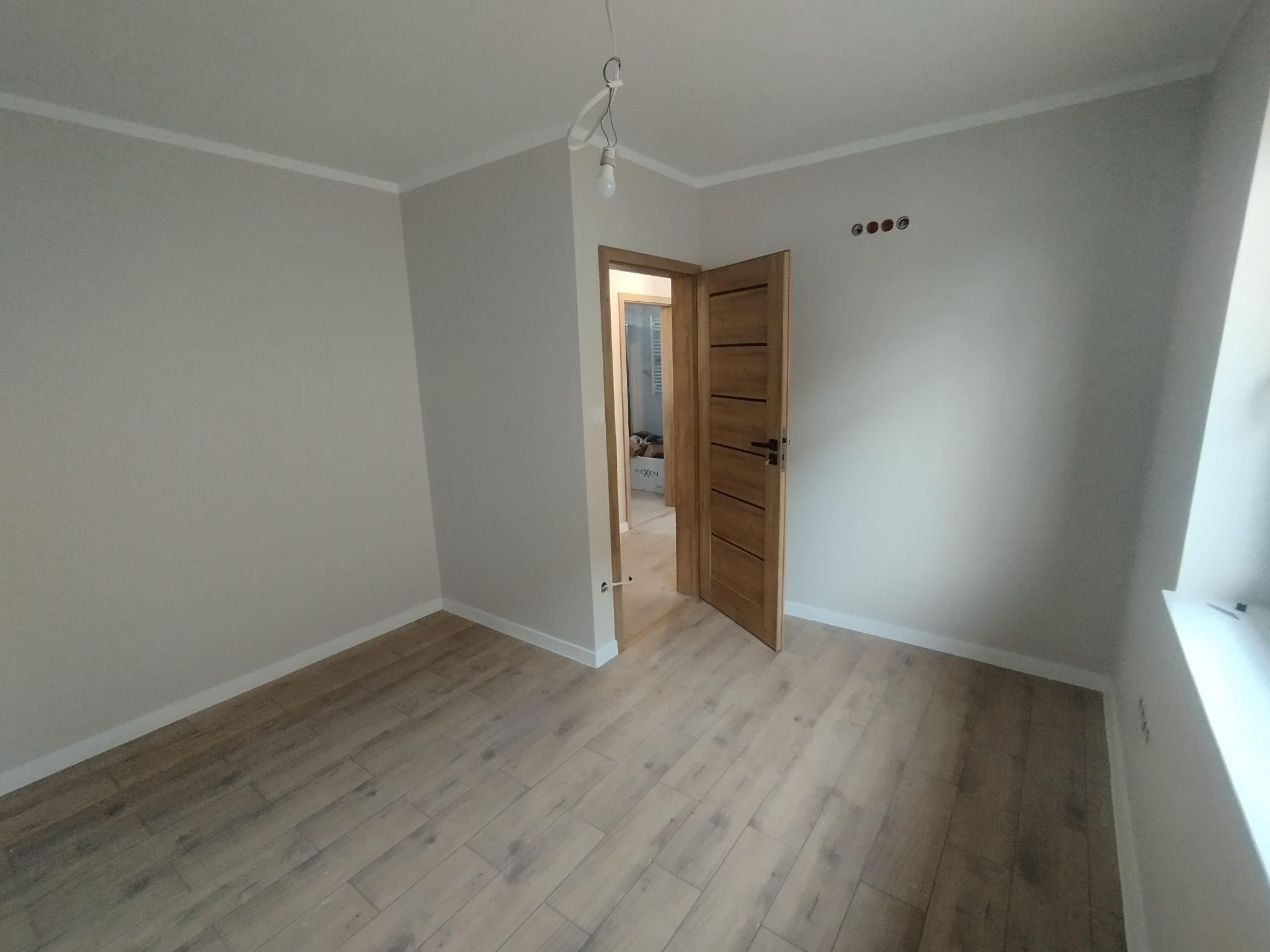 Jasne wnętrze po remoncie w Przecławiu: drewnopodobna podłoga, świeżo pomalowane ściany na szaro, otwarte drewniane drzwi. Widoczne gniazdka elektryczne.