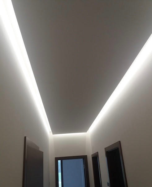 Nowoczesne oświetlenie LED w korytarzu z trzema parami drzwi, listwy LED wpuszczone w sufit tworzą jasne linie.