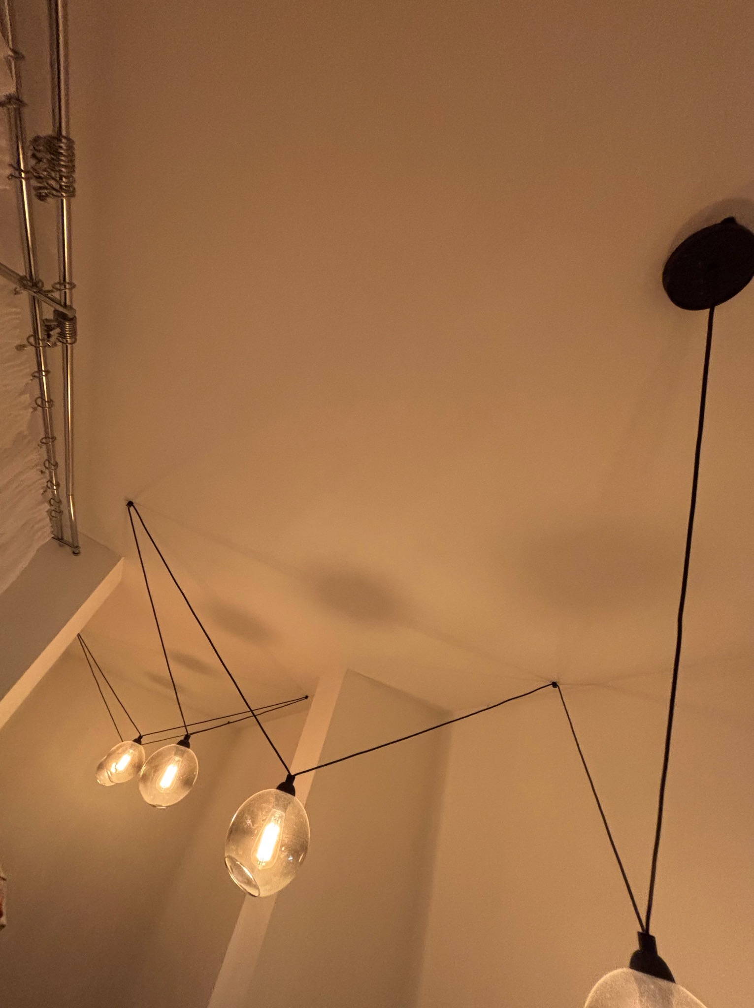 Nowoczesna instalacja oświetleniowa z trzema szklanymi kloszami w kształcie kuli, zawieszonymi na cienkich czarnych przewodach, mocowanych do sufitu za pomocą metalowych elementów. Widoczne również...
