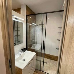 Zrobię Ci Remont Kulig Krystian Usługi Budowlane - Nowoczesna łazienka z kabiną prysznicową typu walk-in z czarnymi profilami, białą umywalką nablatową z drewnianą szafką i lustrem z oświetleniem LED.