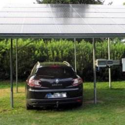 PROZE Jakub Kożuszko - Czarny samochód Renault Megane zaparkowany pod wiatą z paneli słonecznych, z widocznymi inwerterami i zielonym tłem z krzewów.