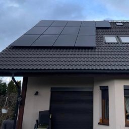 PROZE Jakub Kożuszko - Czarne panele słoneczne na dachu domu z ciemną dachówką, widoczne okna dachowe i czarny komin.