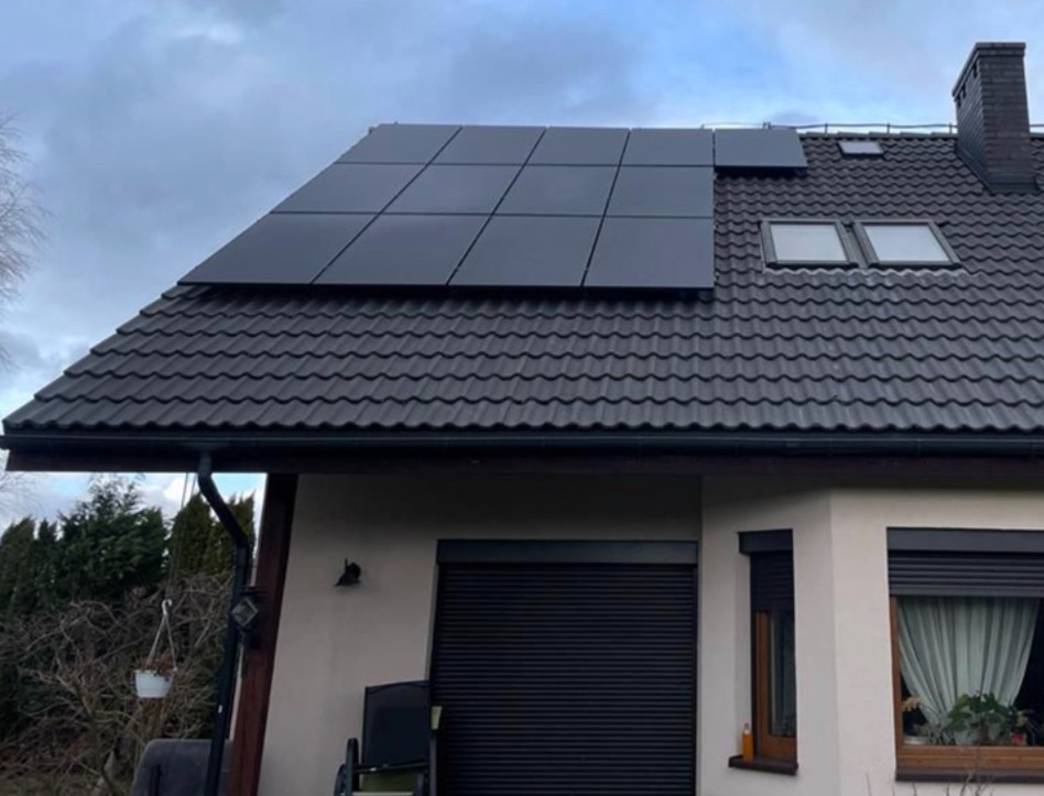 Czarne panele słoneczne na dachu domu z ciemną dachówką, widoczne okna dachowe i czarny komin.