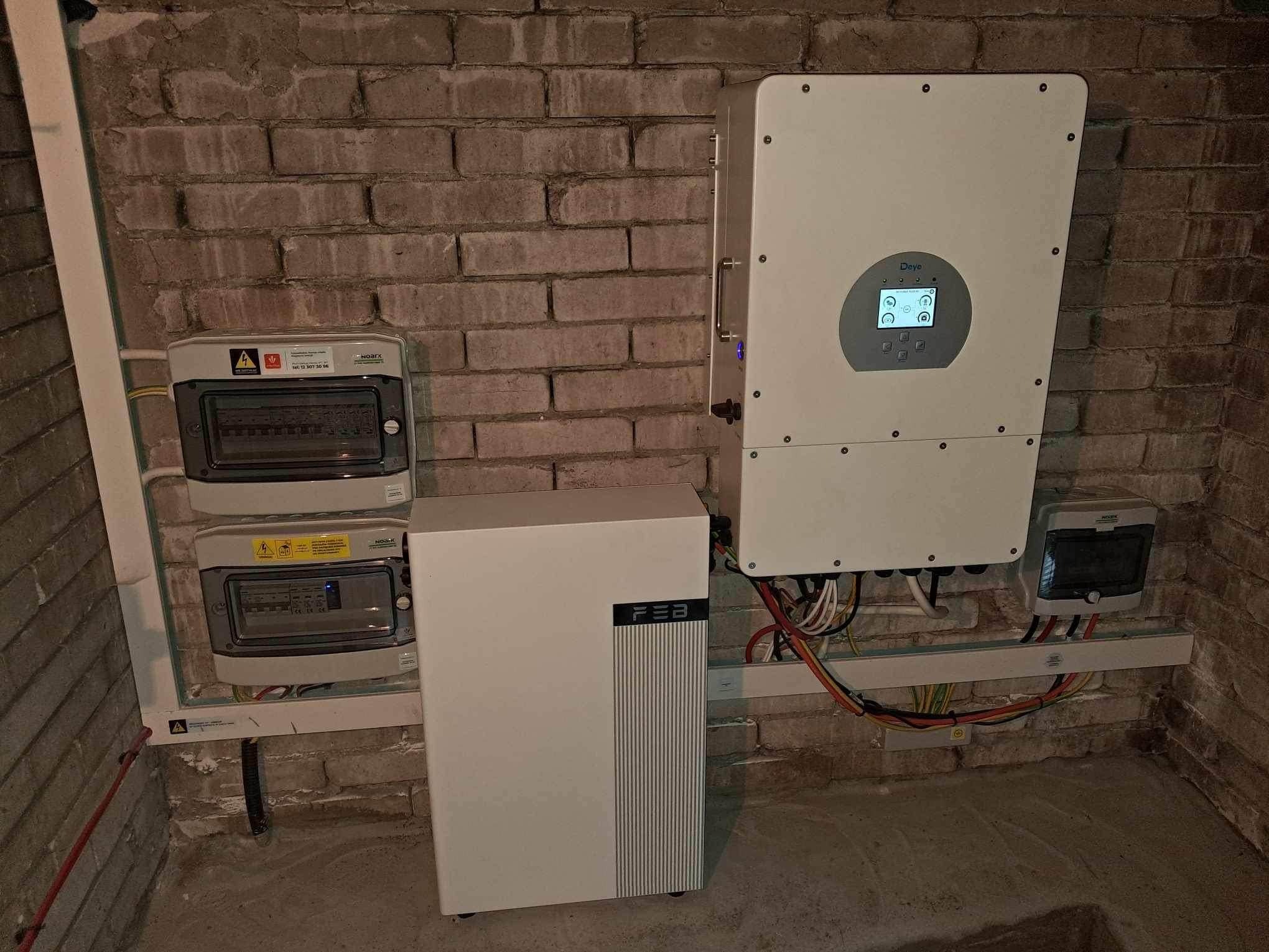 Instalacja wewnętrzna: biały magazyn energii FEB, inwerter Deye z ekranem i skrzynki elektryczne na tle ceglanej ściany w piwnicy.