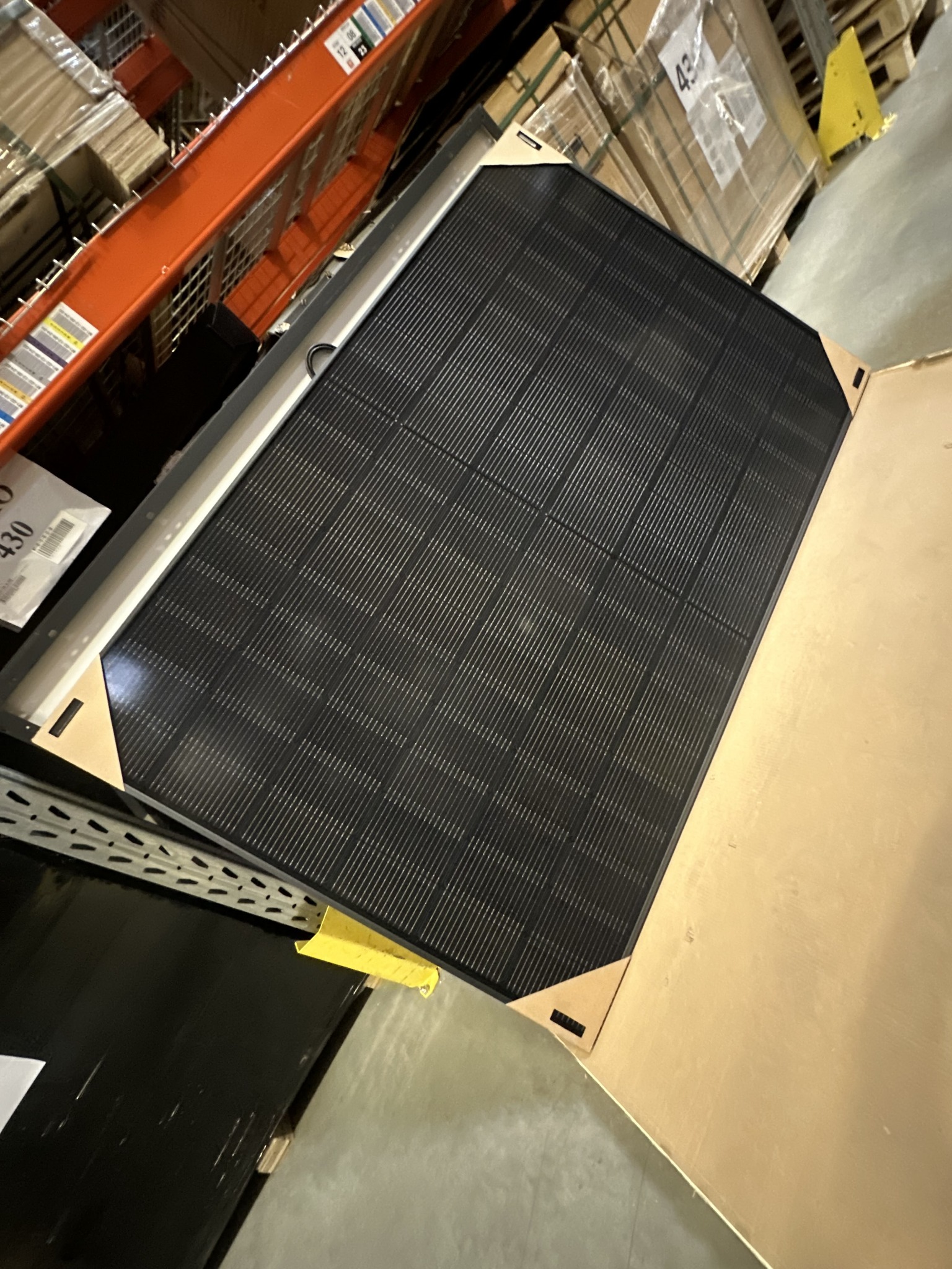 Panel słoneczny w magazynie, zabezpieczony kartonem, widoczny fragment regału magazynowego.