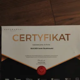 Certyfikat firmy Builder Jacek Skudniewski na drewnianym tle, potwierdzający współpracę z Kaczmarski Group.