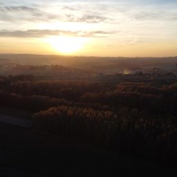 Ordofly - Pejzaż o wschodzie słońca z widokiem na zalesione wzgórza, pola uprawne i oddalony horyzont, sfotografowany z lotu ptaka.