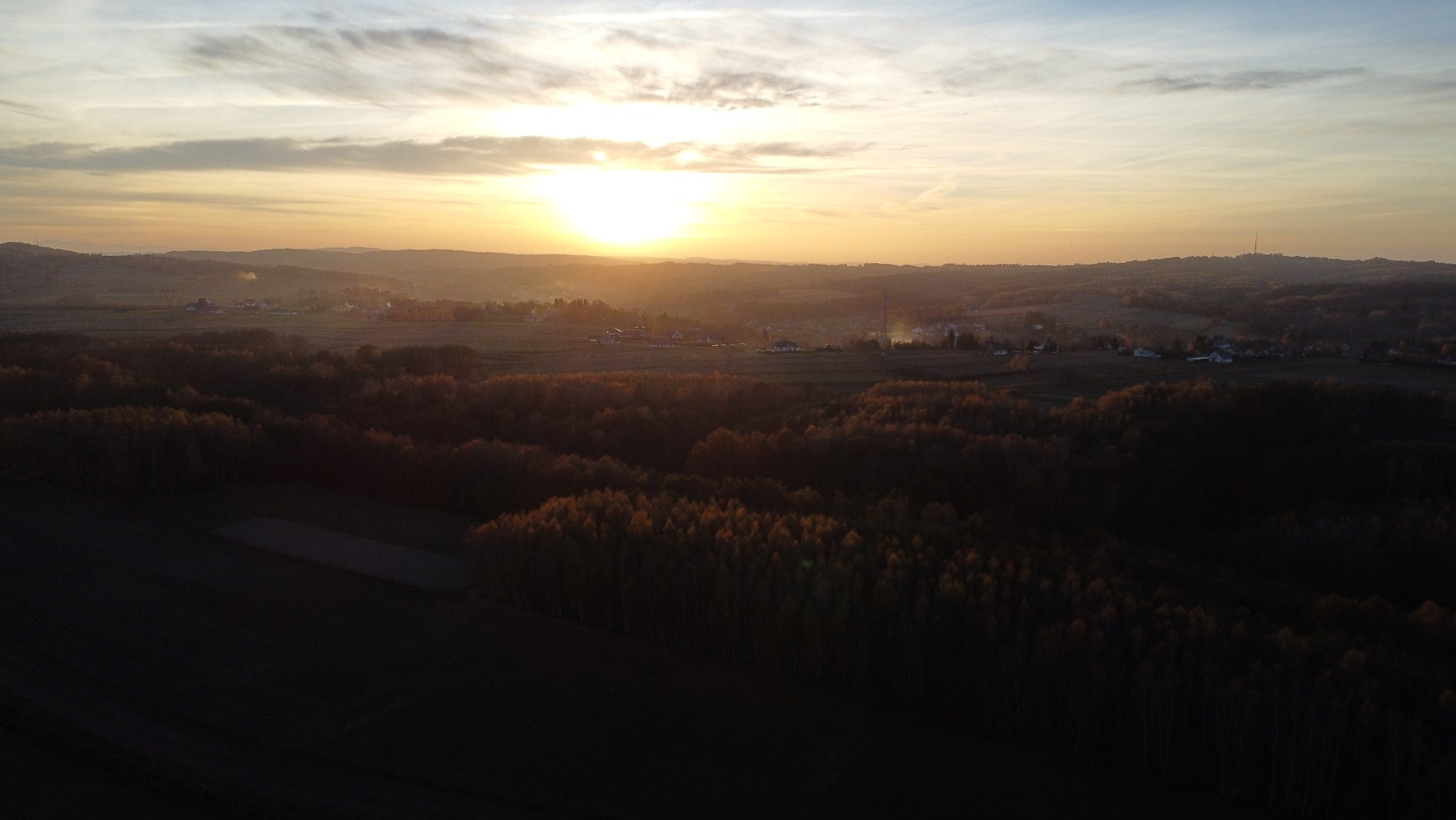 Pejzaż o wschodzie słońca z widokiem na zalesione wzgórza, pola uprawne i oddalony horyzont, sfotografowany z lotu ptaka.