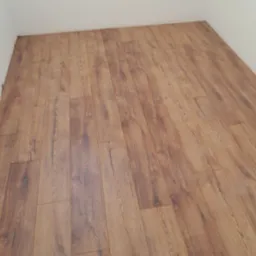 Nowo ułożona podłoga z paneli laminowanych w odcieniach brązu, widoczna z perspektywy narożnika pokoju, z wyraźnym rysunkiem słojów drewna i subtelnymi refleksami światła.