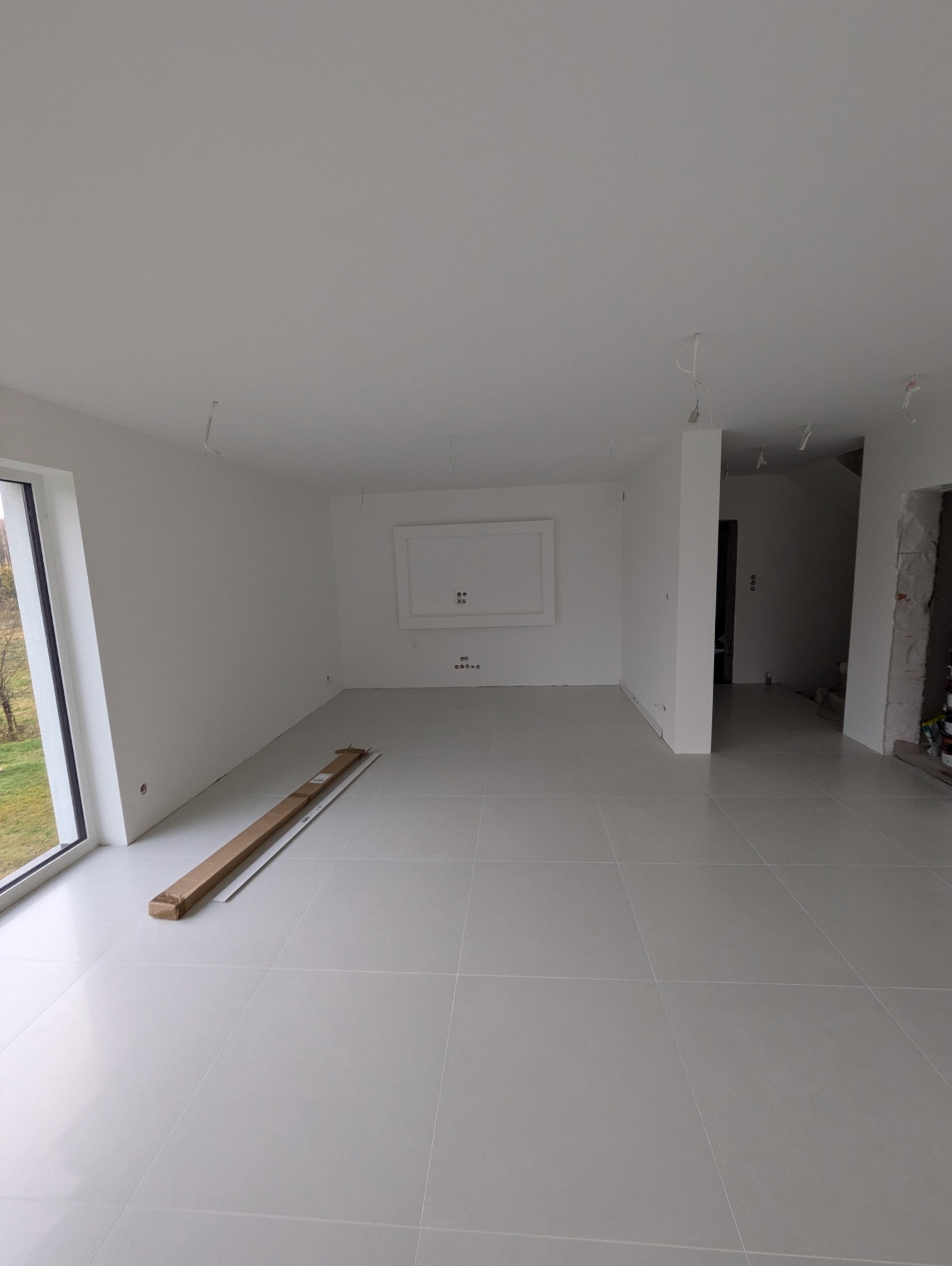 Jasne, przestronne wnętrze w trakcie prac wykończeniowych, z widocznymi świeżo położonymi płytkami podłogowymi, gładkimi, pomalowanymi na biało ścianami i elementami instalacji elektrycznej...