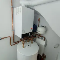 Nowoczesny, biały piec CO marki Viessmann z zasobnikiem wody, widoczne miedziane rury instalacji grzewczej i białe elementy wentylacji w jasnym pomieszczeniu kotłowni.