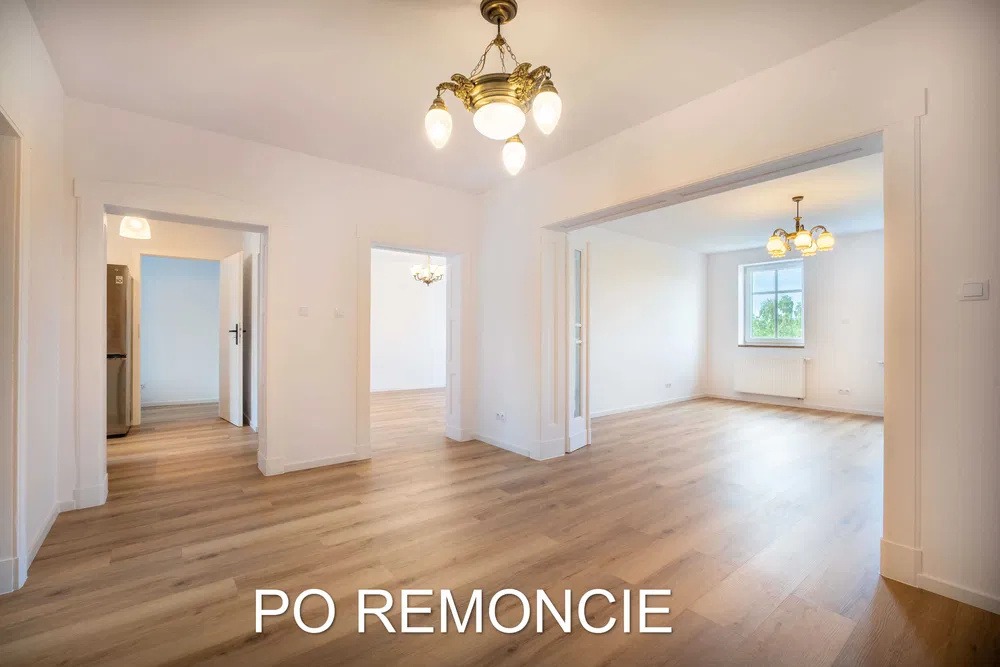 Przestronne wnętrze po remoncie z drewnianą podłogą, białymi ścianami i ozdobnymi lampami wiszącymi, widok na kilka pomieszczeń przez otwarte przejścia.