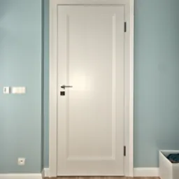 Białe drzwi wewnętrzne z prostokątnym panelem, chromowaną klamką i czarnym zamkiem, na tle błękitnej ściany z białymi listwami przypodłogowymi i drewnianą podłogą.