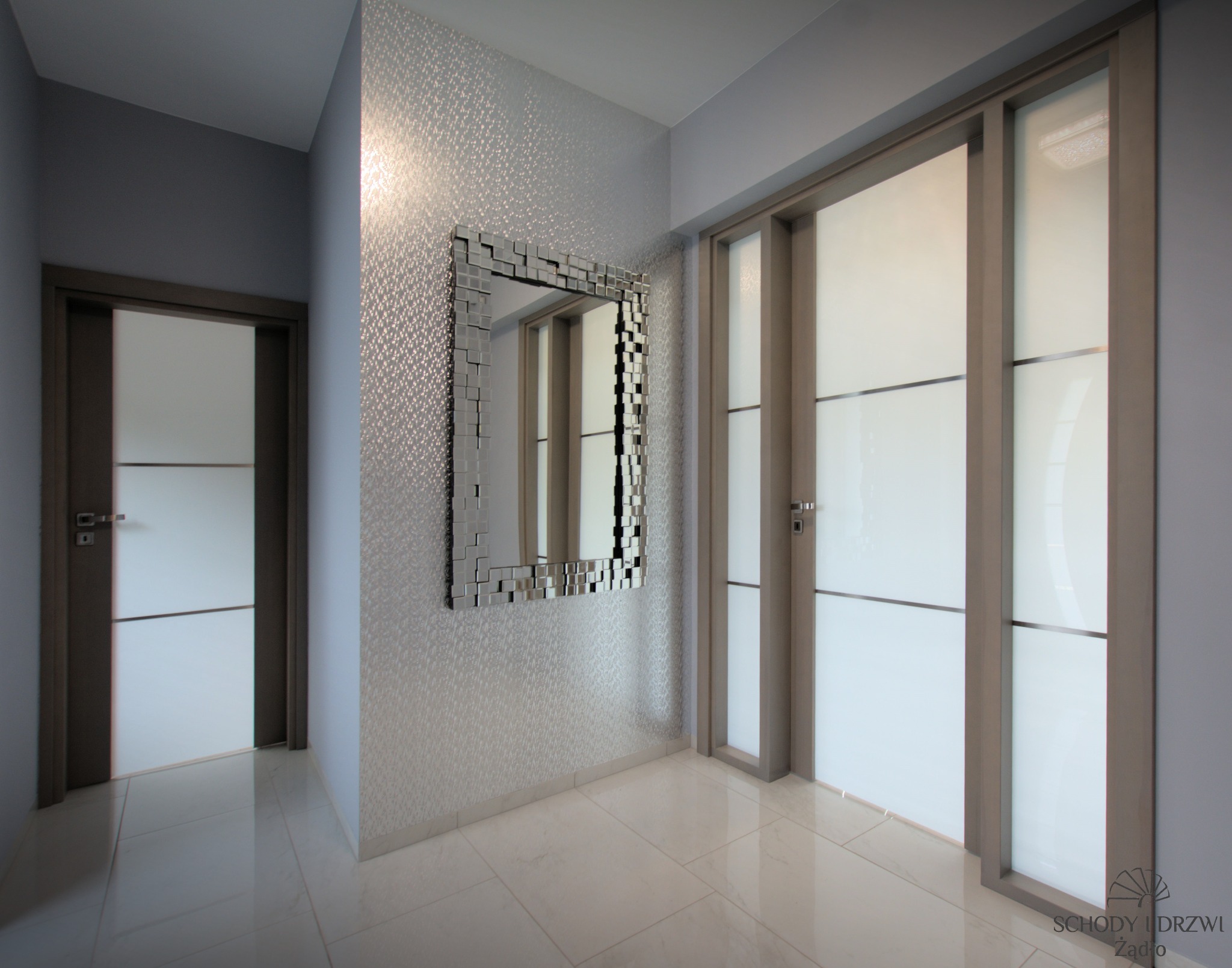 Nowoczesne wnętrze z dwoma parami drzwi przesuwnych z matowego szkła i ciemnymi ramami, lustro z kwadratowych elementów na ścianie z delikatnym wzorem, jasna podłoga z płytek.