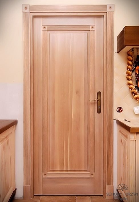 Jasne, drewniane drzwi wewnętrzne z dekoracyjnymi listwami, zamontowane w kuchni z drewnianymi szafkami i ceramiczną dekoracją ścienną.