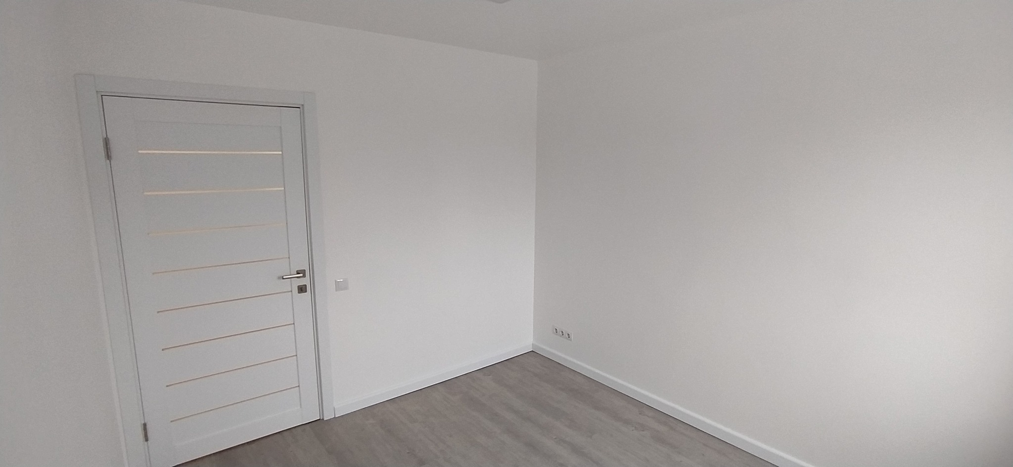 Nowoczesne, białe drzwi wewnętrzne z poziomymi przeszkleniami w wyremontowanym pokoju z szarymi panelami podłogowymi i świeżo pomalowanymi na biało ścianami.