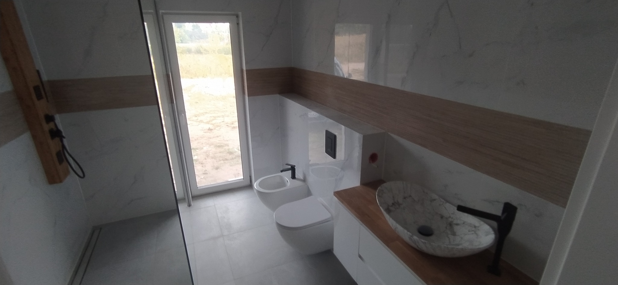 Nowoczesna łazienka z marmurowymi płytkami, drewnianymi akcentami i designerską umywalką w kształcie łzy.