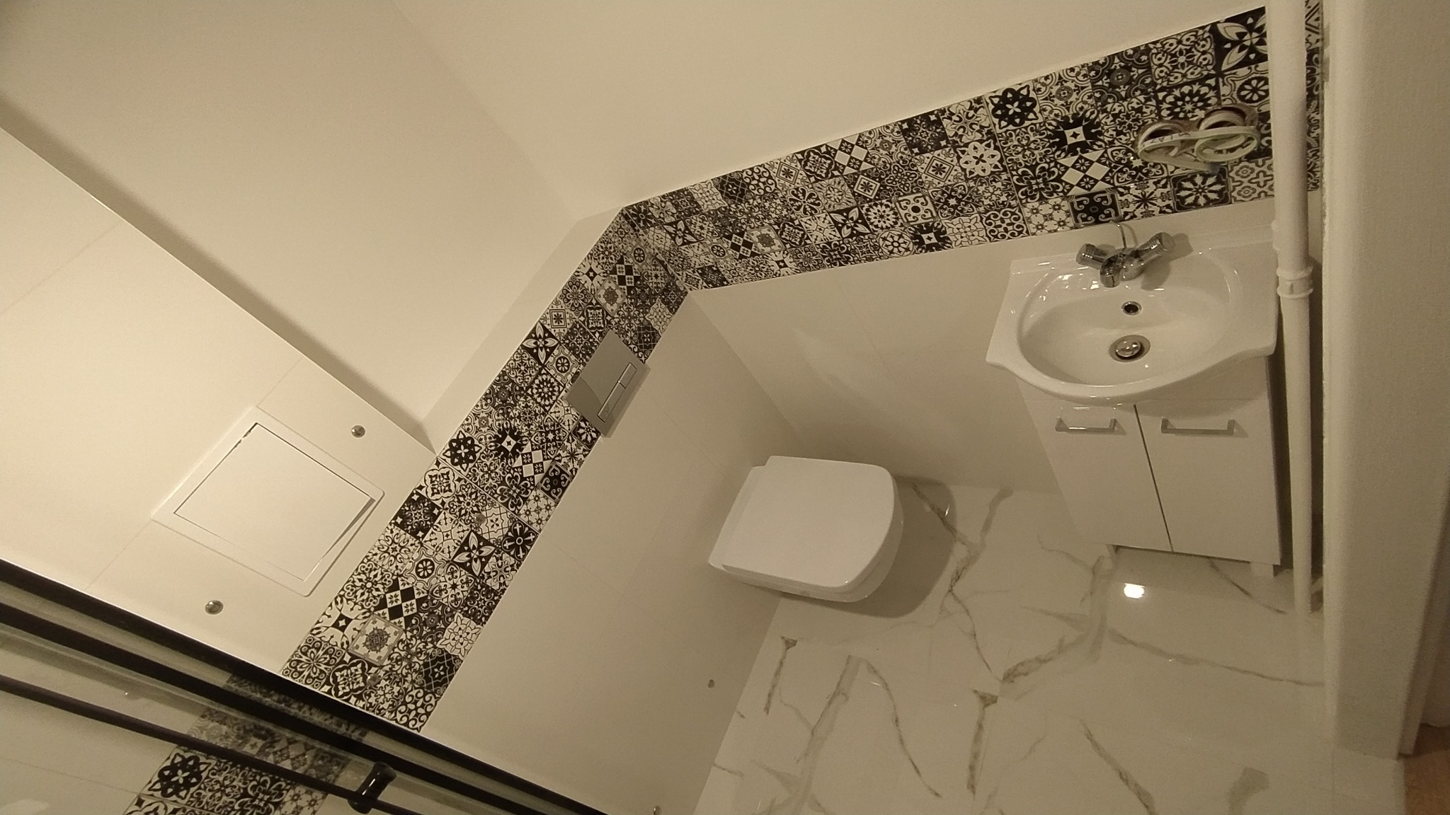 Nowoczesna łazienka z białymi sanitariatami, wzorzystymi płytkami dekoracyjnymi i marmurową podłogą, widok z góry.