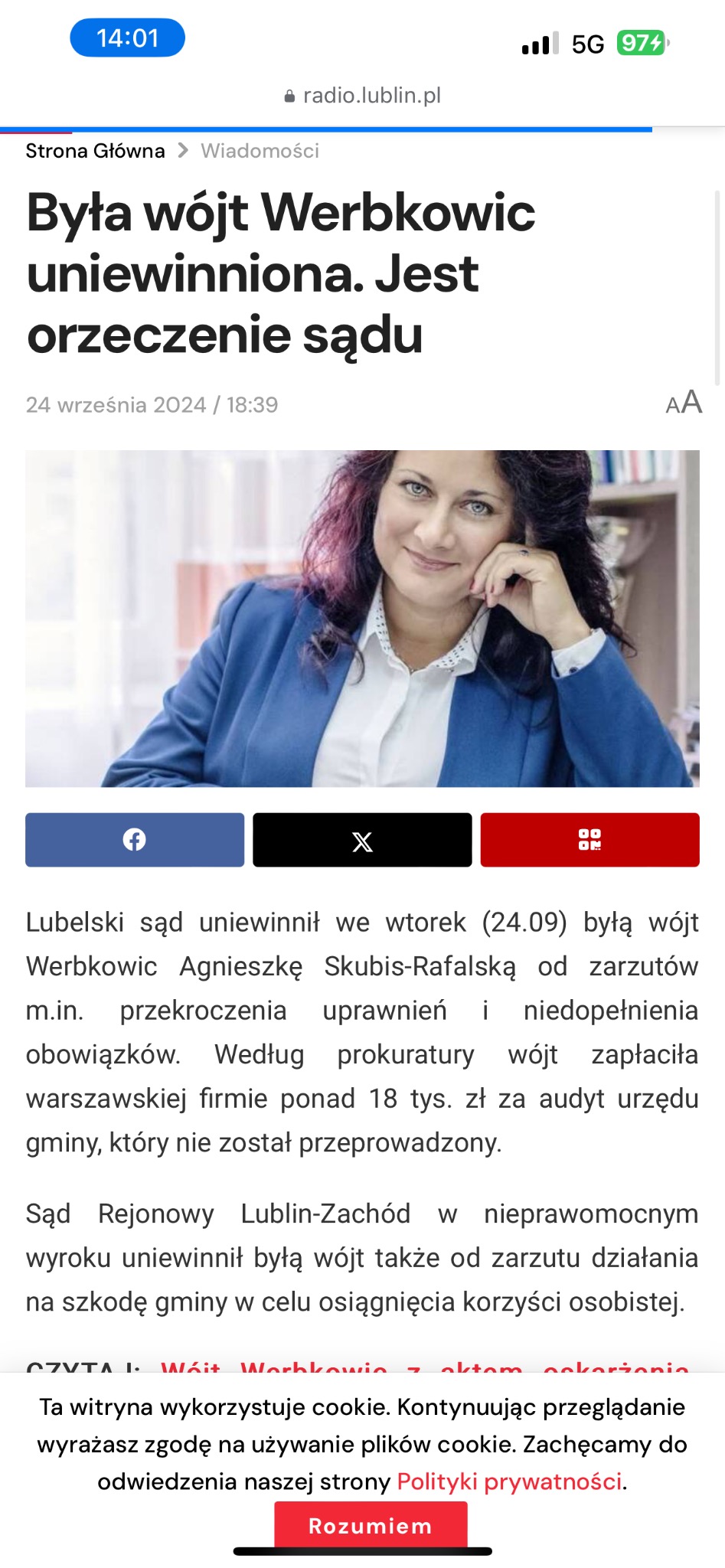Portret uśmiechniętej kobiety w niebieskiej marynarce, opierającej brodę na dłoni, z widocznymi książkami w tle.