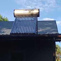 Piotr Orzechowicz - Kolektor słoneczny rurowo-próżniowy zamontowany na dachu budynku, widoczny zbiornik ze stali nierdzewnej z logo producenta, błękitne niebo w tle.