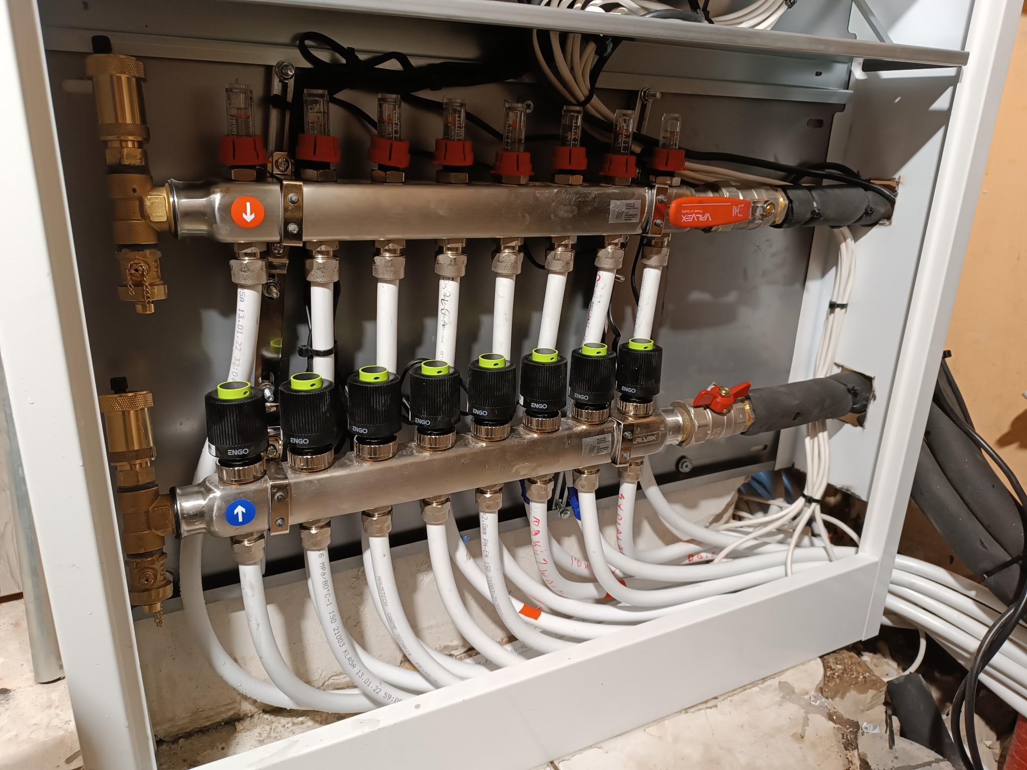 Rozdzielacz podłogowy w szafce, widoczne zawory z przepływomierzami, rury doprowadzające i odprowadzające wodę, instalacja w trakcie montażu.