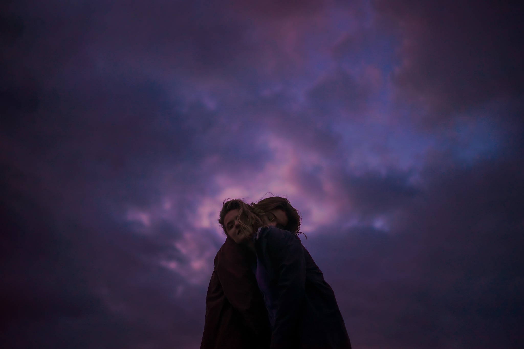 Silueta zakochanej pary na tle dramatycznego, fioletowego nieba o zmierzchu. Ujęcie z dołu podkreśla bliskość i intymność chwili.