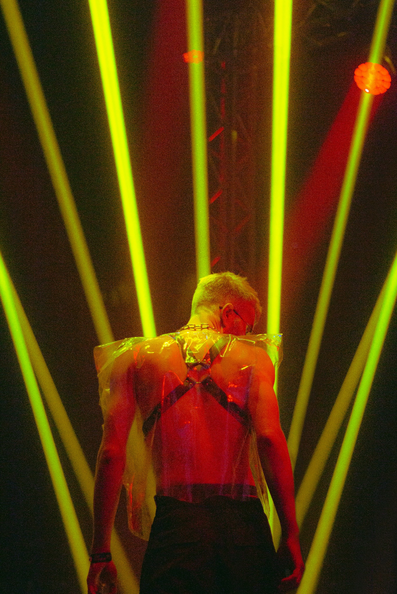 Osoba w artystycznym oświetleniu na evencie w Warszawie. Nietypowy strój i intensywne barwy tworzą unikalną atmosferę.