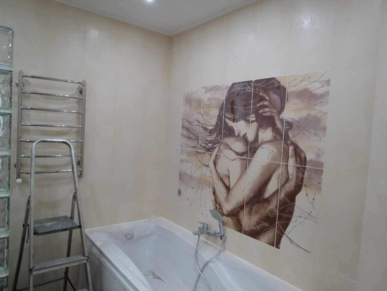 Wykończona łazienka z beżowymi płytkami, na ścianie mozaika z wizerunkiem pary, drabinka i aluminiowa drabina obok wanny.