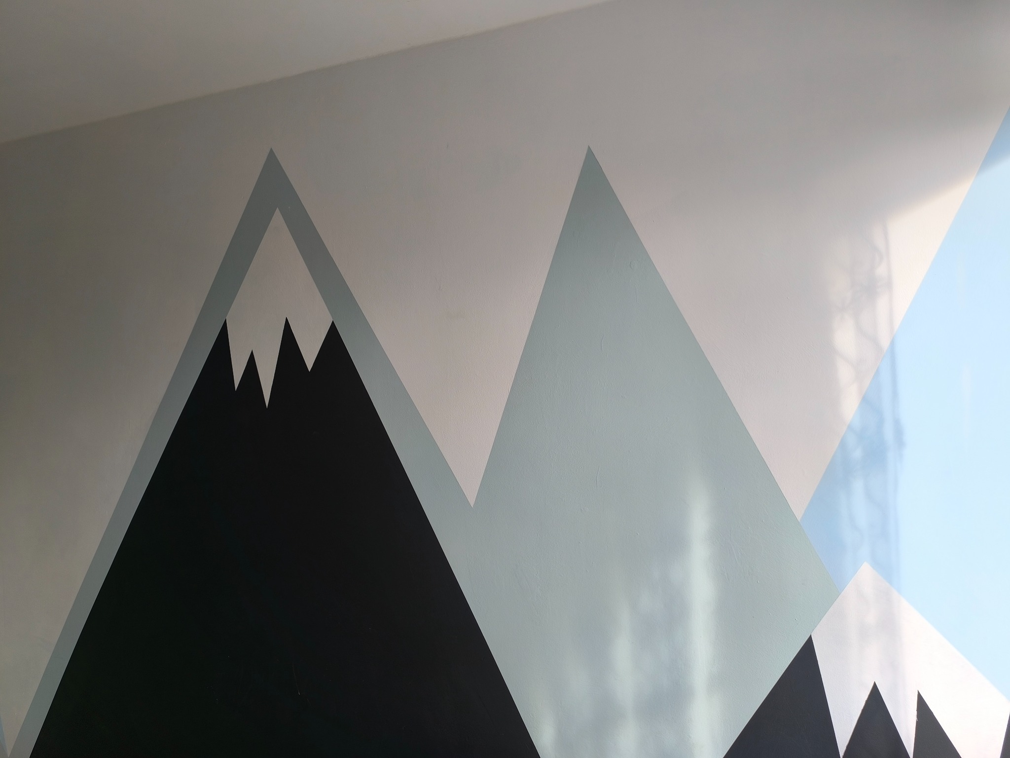 Geometryczny wzór gór w odcieniach szarości, bieli i czerni, namalowany na ścianie w pokoju.