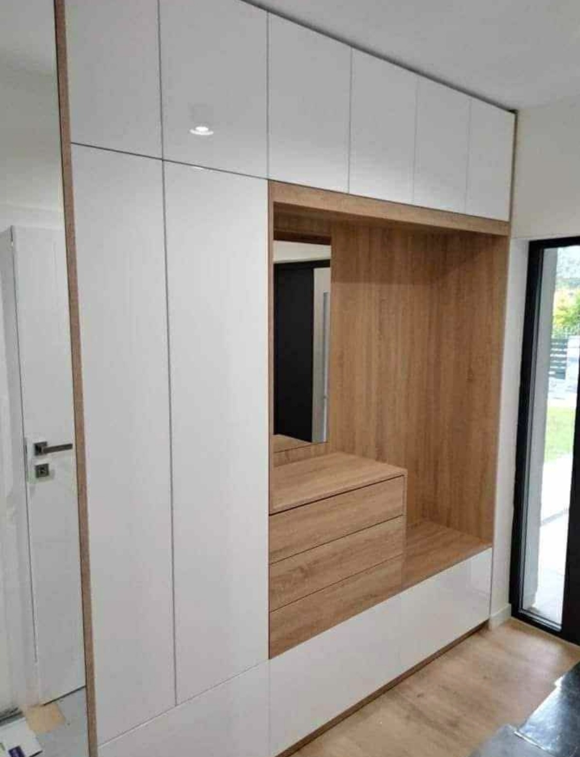 Biało-drewniana szafa wnękowa z lustrem i szufladami, wykonana na wymiar w Żarkach. Nowoczesny design, jasne kolory, minimalistyczne uchwyty.