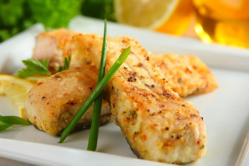 Apetyczne filety rybne z przyprawami na białym talerzu, udekorowane zieleniną i cytryną. Profesjonalny catering we Wrocławiu.