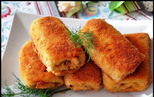 Apetyczne krokiety na białym talerzu, udekorowane zielonym koperkiem, na tle kolorowej serwety. Idealne danie na catering okolicznościowy lub firmowy.