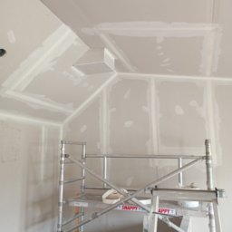 Malermester RAF Wojciechowski - Sufit poddasza wykończony płytami kartonowo-gipsowymi, widoczne łączenia szpachlowane, na pierwszym planie aluminiowe rusztowanie z narzędziami.