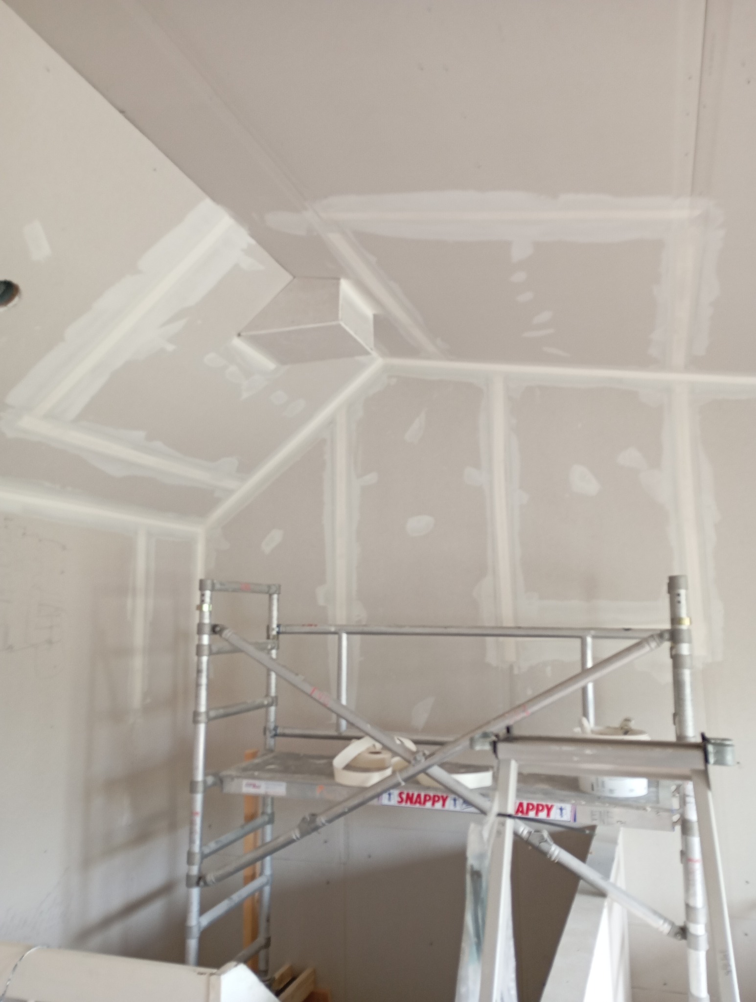 Sufit poddasza wykończony płytami kartonowo-gipsowymi, widoczne łączenia szpachlowane, na pierwszym planie aluminiowe rusztowanie z narzędziami.